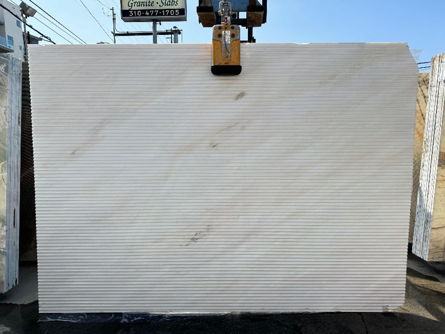 Large slab of white marble being lifted by a crane with a blue sky in the background.